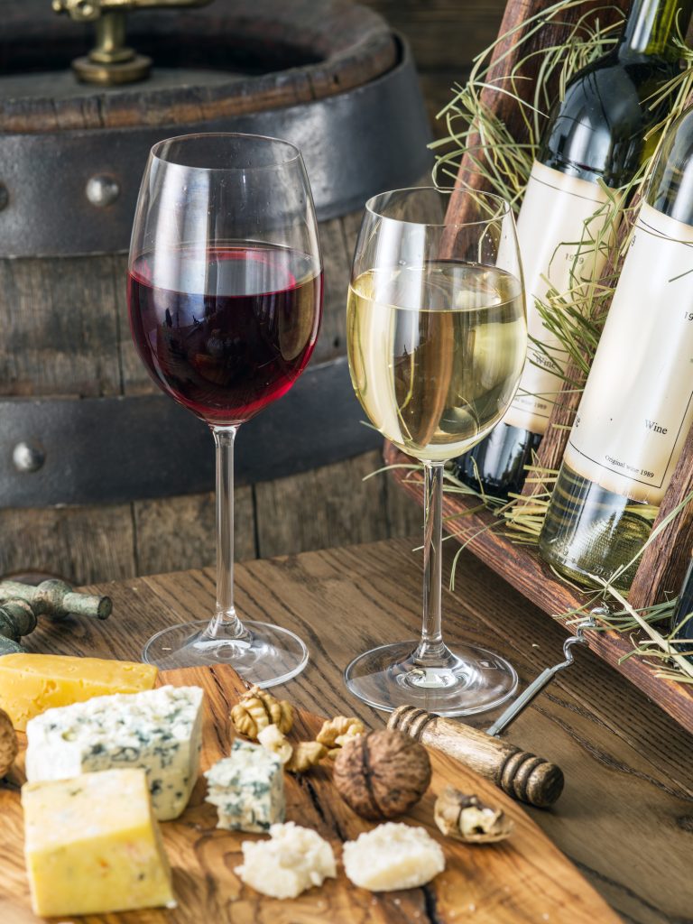 two glasses of wine with soft cheese laid out and an open display box of wine bottles in the background