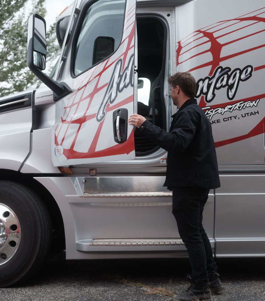 Driver dressed in black opening the door of a white Advantage Transportation truck